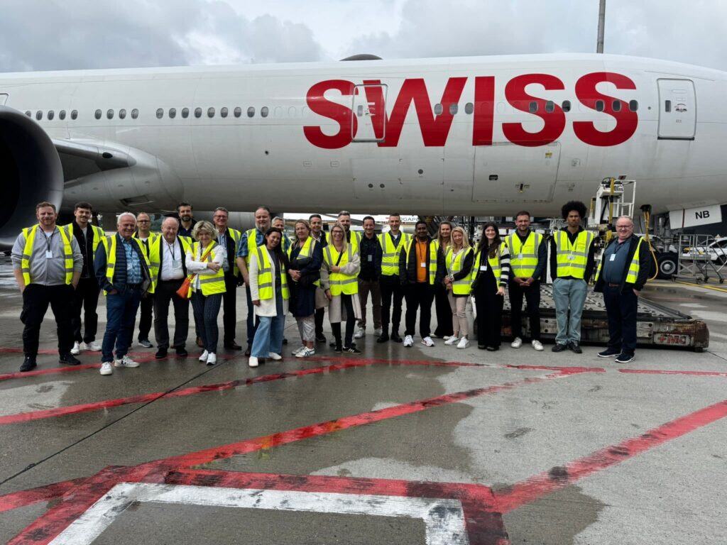 Airline crew and staff posed for a group photo at the airport with large Swiss airplane in background.