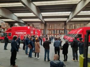 Red SMA moving trucks at an indoor event with people gathered around; branding visible.