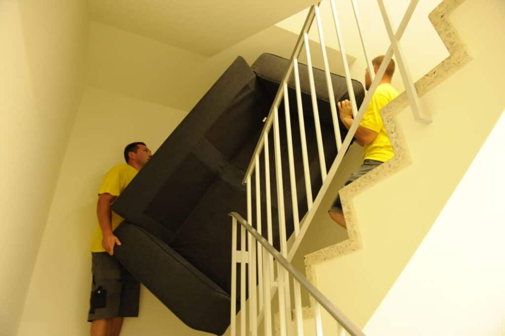 Efficient moving team carrying a large sofa up the staircase for residential relocation.