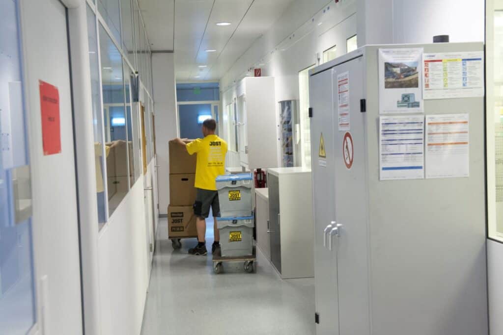 Pest control technician moving boxes in medical facility corridor.