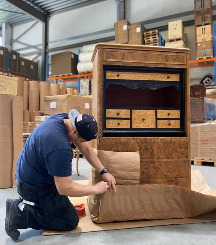Handyman wrapping antique wooden cabinet in protective paper for furniture moving and assembly services.